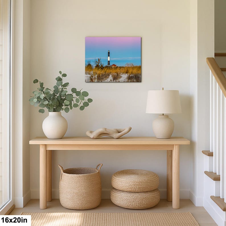 Op de afbeelding: Een 40x50 cm canvas print van een vuurtoren op het strand. De vuurtoren is zwart en wit, tegen een blauwe lucht en roze zonsondergang. De sc&egrave;ne omvat zandduinen en een houten hek.