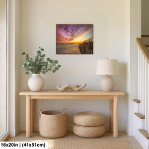 Peut inclure: Tableau encadr&eacute; de 41x51cm repr&eacute;sentant une sc&egrave;ne de plage au coucher du soleil. L'&oelig;uvre pr&eacute;sente un ciel color&eacute;, une plage de sable et une cl&ocirc;ture en bois. Le tableau est expos&eacute; au-dessus d'une console en bois.