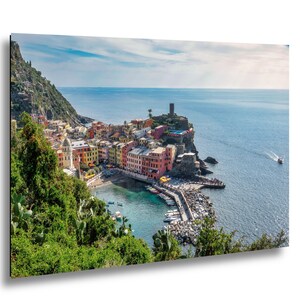 May include: A vibrant coastal town print featuring colorful buildings nestled along a rocky coastline. The image showcases a harbor filled with boats, a stone pier, and a clear blue sea under a bright sky. A picturesque landscape scene.