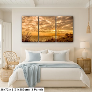 May include: A three-panel canvas print depicting a sunset over water. The sky is filled with golden clouds, and the sun's rays burst through. The print measures 36x72 inches.