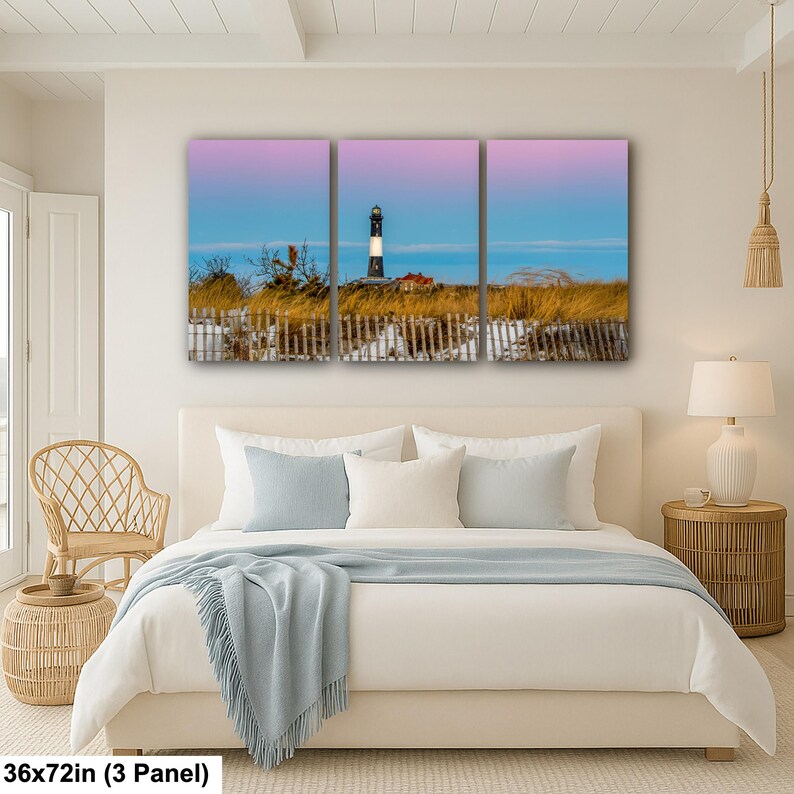 Op de afbeelding: Een drieluik canvas print met een kustlandschap. Het kunstwerk toont een vuurtoren met zwart-witte strepen tegen een roze en blauwe lucht. De afmetingen zijn 91x183 cm.