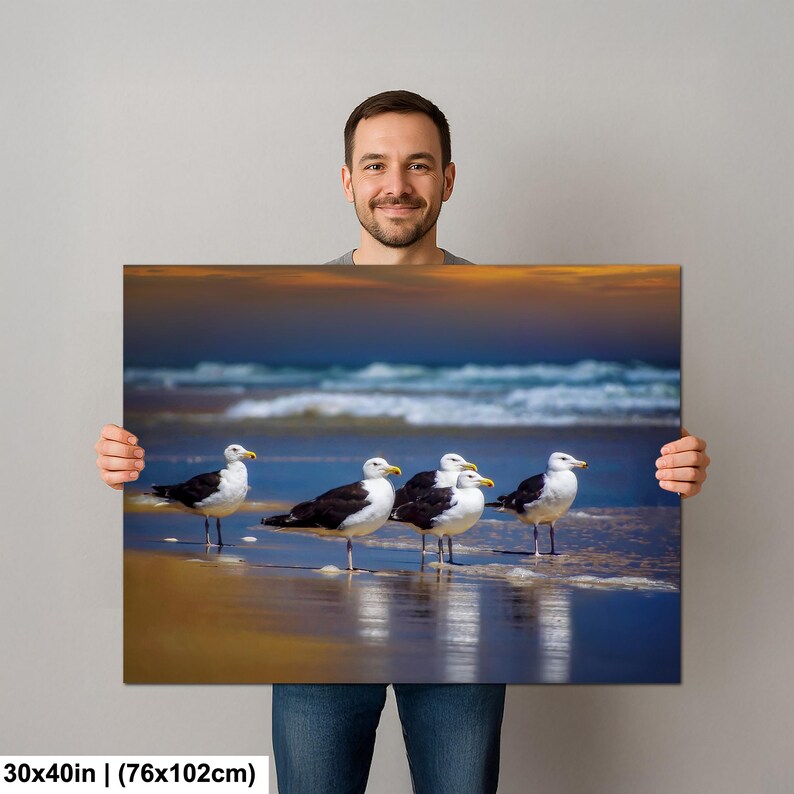 Może przedstawiać: Obraz na pł&oacute;tnie o wymiarach 76x102cm przedstawiający pięć mew na plaży. Ptaki mają czarno-białe upierzenie i ż&oacute;łte dzioby, na tle fal oceanu i zachodu słońca.