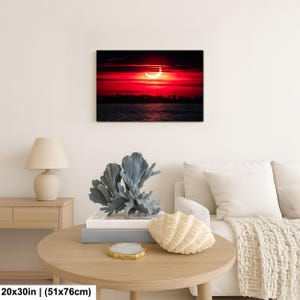 Pode incluir: Impress&atilde;o em tela emoldurada retratando um eclipse solar sobre a &aacute;gua. O c&eacute;u &eacute; vermelho vibrante com um sol em forma de crescente. A impress&atilde;o mede 51 cm x 76 cm.