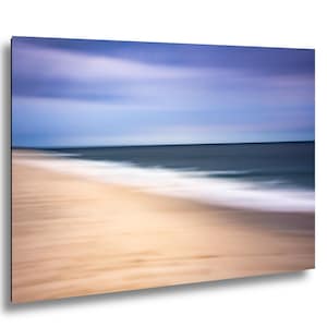 May include: Abstract beach scene with blurred motion. The image features a sandy beach in the foreground, transitioning to the ocean and sky. The colors include shades of tan, blue, and white, creating a sense of tranquility.