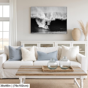 K&ouml;nnte beinhalten: Schwarz-Wei&szlig;-Leinwanddruck eines Surfers auf einer Welle. Das Kunstwerk wird &uuml;ber einem wei&szlig;en Sofa mit blauen und wei&szlig;en Kissen gezeigt. Der Raum verf&uuml;gt au&szlig;erdem &uuml;ber einen Holztisch und dekorative Vasen.