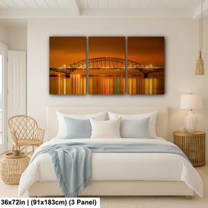 May include: A three-panel canvas print depicting a bridge at night, with the bridge's lights reflected in the water below. The artwork measures 36x72 inches. The color palette is dominated by warm oranges and yellows, creating a serene and atmospheric scene.