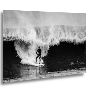 K&ouml;nnte beinhalten: Schwarz-Wei&szlig;-Fotografie eines Surfers auf einem Surfbrett, der eine riesige Welle reitet. Der Surfer, in einem dunklen Neoprenanzug, ist in Bewegung. Das Bild f&auml;ngt die Kraft und Dynamik des Ozeans ein.