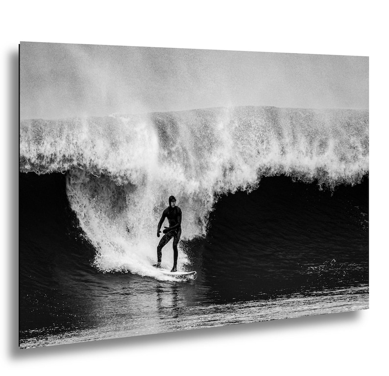 K&ouml;nnte beinhalten: Schwarz-Wei&szlig;-Fotografie eines Surfers auf einem Surfbrett, der eine riesige Welle reitet. Der Surfer, in einem dunklen Neoprenanzug, ist in Bewegung. Das Bild f&auml;ngt die Kraft und Dynamik des Ozeans ein.