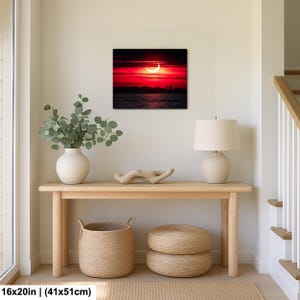 Pode incluir: Impress&atilde;o em tela quadrada de 41x51cm retratando um p&ocirc;r do sol dram&aacute;tico sobre a &aacute;gua. O c&eacute;u &eacute; vermelho intenso com uma forma de lua crescente. A impress&atilde;o &eacute; exibida acima de uma mesa de console de madeira.