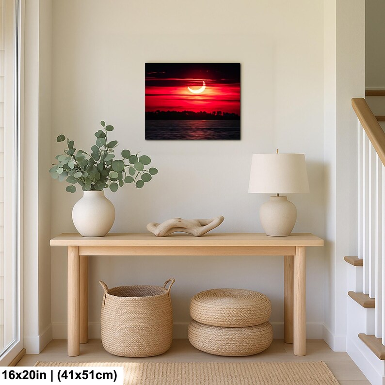 Pode incluir: Impress&atilde;o em tela quadrada de 41x51cm retratando um p&ocirc;r do sol dram&aacute;tico sobre a &aacute;gua. O c&eacute;u &eacute; vermelho intenso com uma forma de lua crescente. A impress&atilde;o &eacute; exibida acima de uma mesa de console de madeira.