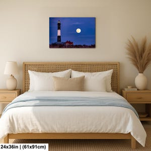 May include: A canvas print of a lighthouse under a full moon. The lighthouse is black and white with a red roofed building next to it. The print is 24x36 inches.