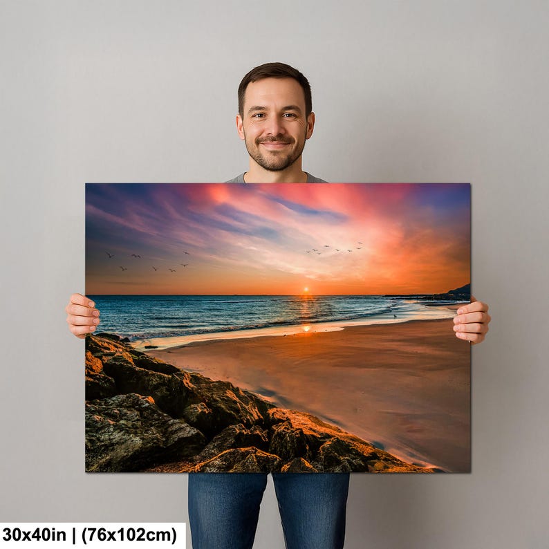 May include: A canvas print depicting a beach scene at sunset. The artwork features a vibrant sky with orange, pink, and purple hues, reflecting on the ocean. The dimensions are 30x40 inches (76x102cm).
