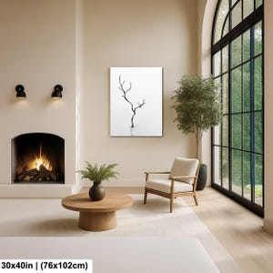 May include: A minimalist interior scene featuring a framed black and white art piece depicting a bare tree. The artwork is 30x40 inches (76x102cm). The room includes a fireplace, a round wooden coffee table, and a modern armchair.
