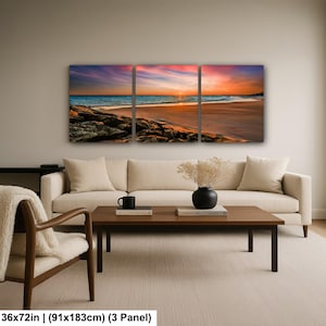 May include: A three-panel canvas print depicting a beach scene at sunset. The sky is a blend of orange, pink, and purple hues, reflecting on the water. The print measures 36x72 inches (91x183cm).