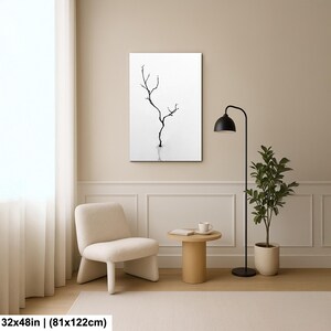 May include: A black and white minimalist art print featuring a bare tree silhouette. The artwork is rectangular, measuring 32x48 inches (81x122cm), and hangs on a neutral-toned wall. The room includes a chair, side table, floor lamp, and potted plant.