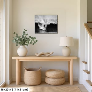 K&ouml;nnte beinhalten: Schwarz-Wei&szlig;-Druck eines Surfers auf einer Welle, 41x51cm gro&szlig;. &Uuml;ber einer hellen Holzkonsolentisch mit wei&szlig;er Vase, Lampe und geflochtenen K&ouml;rben.