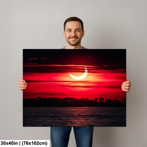 Pode incluir: Uma impress&atilde;o em tela com um vibrante p&ocirc;r do sol vermelho com um eclipse solar em forma de crescente. A obra de arte retrata um corpo de &aacute;gua e uma linha de &aacute;rvores em silhueta. A impress&atilde;o mede 76x102cm.