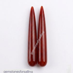 May include: Two smooth, polished, deep red gemstone points with a tapered, elongated shape. The text gemstonesforsalling is printed vertically along the right piece and horizontally at the bottom left of the image. The stones have a glossy finish.