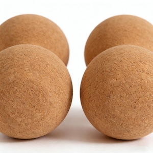 May include: Four spherical cork balls are arranged against a white background. The balls are a light brown color and have a textured surface. The balls are evenly spaced and appear to be made of natural cork material.