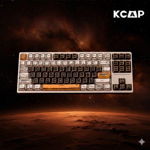 May include: A white and gold mechanical keyboard with black keycaps. The keyboard has a unique design with illustrations on the keys and the text "KCAP" in the upper right corner. The background features a space-themed design with a planet and stars.