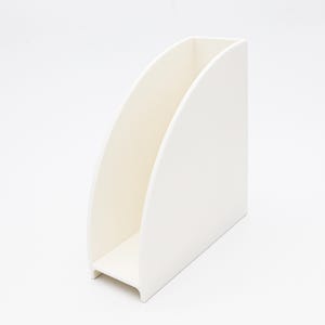 May include: A white, minimalist magazine holder with a curved design. The holder is made of a solid, opaque material and features a rectangular base. The interior is a slightly off-white color, creating a subtle contrast.
