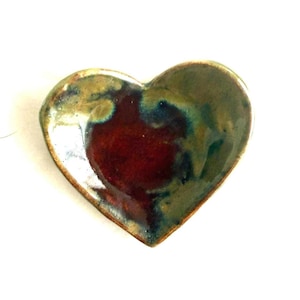 May include: Heart-shaped ceramic dish with a glossy finish. The dish features a rich, dark red center, transitioning to shades of green and brown around the edges. The heart-shaped design is perfect for holding small items.