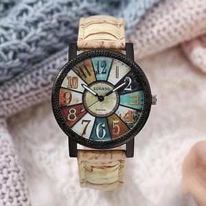 May include: A round wristwatch with a black bezel and a colorful face featuring large numerals. The watch has a light-colored band with a textured pattern. The watch face displays the brand name "SOTUKDO".