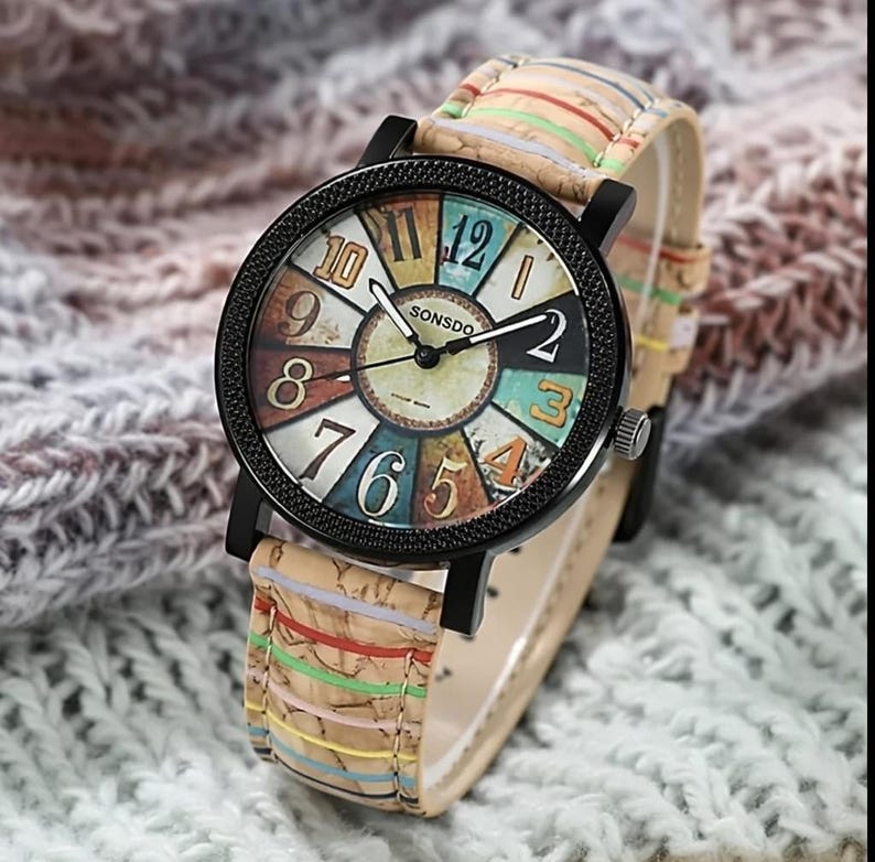 May include: A wristwatch with a black bezel and a colorful face featuring the text "SONSDO". The watch has a beige band with colorful stripes. The watch face displays the numbers 1 through 12.