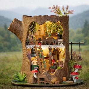 Peut inclure: Une maison de poupée miniature en forme de souche d'arbre avec éclairage intérieur. L'extérieur marron présente une texture d'écorce détaillée, avec une échelle, une balançoire et des accents de champignons rouges. L'intérieur est meublé et végétalisé.