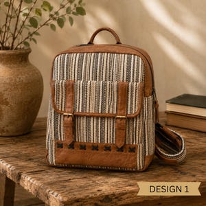 May include: A backpack featuring a woven striped pattern in shades of brown, cream, and black. It includes brown faux leather trim, two front buckle straps, a top handle, and a decorative cross-stitch detail along the bottom. Text reads DESIGN 1.