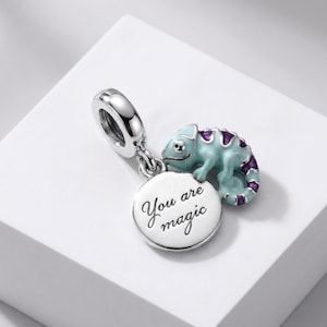 May include: A silver charm featuring a light blue and purple enamel chameleon perched next to a circular silver disc. The disc is engraved with the black text You are magic. The charm includes a polished silver bail for attachment to a bracelet.