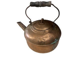 Peut inclure: Bouilloire ancienne en cuivre avec une poignée en bois foncé. La bouilloire a un bec verseur et un couvercle avec un petit bouton. Le cuivre présente une patine, montrant des signes d'âge. La poignée est fixée avec des supports métalliques.