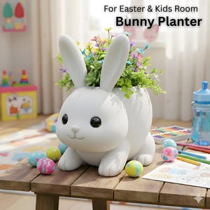Könnte beinhalten: Ein weißer Hasen-Blumentopf gefüllt mit bunten Blumen. Der Pflanztopf hat große Ohren und ein lächelndes Gesicht. Ostereier sind auf dem Holztisch verstreut. Der Text "For Easter & Kids Room Bunny Planter" ist sichtbar.