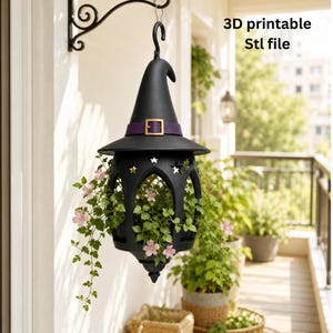 May include: A black hanging planter shaped like a witch hat with a purple band and gold buckle, featuring star-shaped cutouts and a pointed top. The planter holds green foliage with small pink flowers. Text reads: 3D printable Stl file.