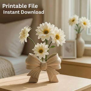 Puede incluir: Un jarrón de cerámica beige con forma de lazo, que contiene flores blancas con centros amarillos. El jarrón está sobre una superficie de madera. El texto "Printable File Instant Download" está en la parte superior.
