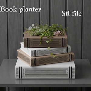Può includere: Una pila di quattro fioriere a forma di libro, ciascuna di un colore diverso: bianco, beige e marrone. La fioriera superiore contiene varie piante grasse e piante ricadenti. Il testo "Book planter" e "Stl file" sono visibili.