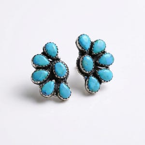 May include: A pair of turquoise cluster earrings. Each earring features multiple teardrop-shaped, bright blue turquoise stones set in a silver-colored metal. The earrings are designed to be worn on the earlobes.
