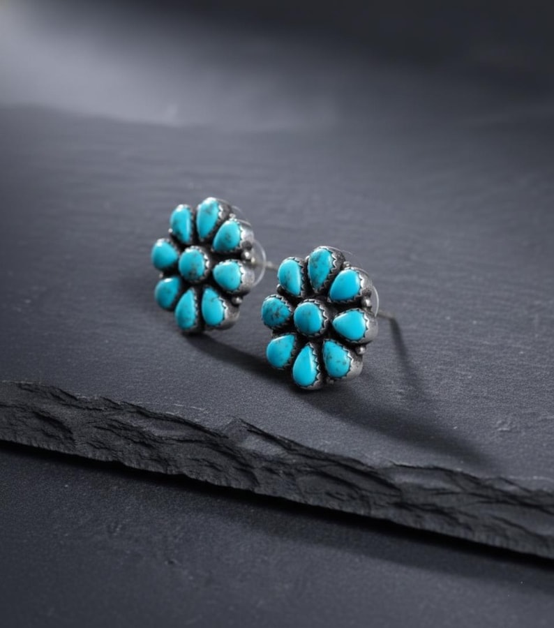May include: A pair of silver stud earrings with a floral design. Each earring has a cluster of turquoise-coloured, teardrop-shaped stones. The earrings are set against a dark background, highlighting the bright blue stones.