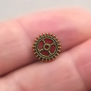 May include: A small gold-coloured gear charm with a red centre. The gear is a popular steampunk design element.