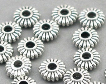 May include: A collection of silver-toned metal beads with a flower-shaped design. The beads have a small hole in the center for stringing.