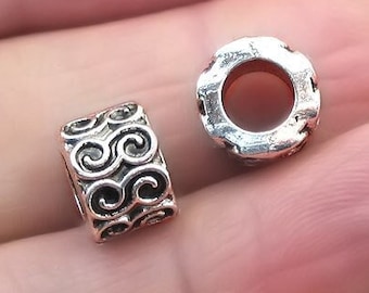 May include: Two silver metal bead spacers with an intricate swirl design. The spacers are designed to be used in jewellery making.