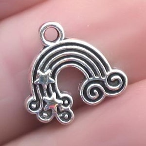 May include: Silver charm with a rainbow design and stars. The rainbow has a textured surface and the stars are raised. The charm has a loop at the top for attaching to a necklace or bracelet.