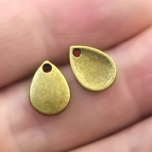 May include: Two antique gold-toned metal teardrop-shaped charms with a hole at the top for stringing.