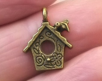 May include: A bronze-colored birdhouse charm with a small bird perched on the roof. The birdhouse has a detailed design with swirls and flowers.