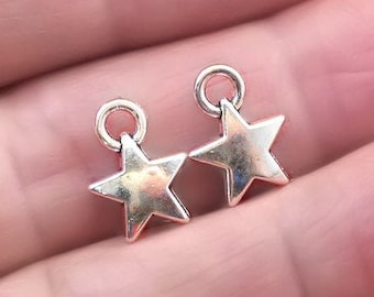 May include: Two silver star-shaped charms with jump rings. The charms are on a hand.