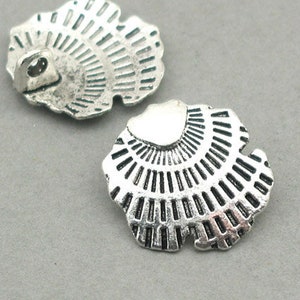 Peut inclure: Deux embellissements décoratifs en métal argenté en forme de coquillages avec un motif en éventail.