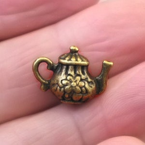 May include: A small gold-toned teapot charm with a floral design. The charm is about the size of a dime.