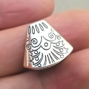 May include: Silver-toned metal pendant with a decorative, geometric design. The pendant is shaped like a triangle with rounded edges and features a detailed, intricate pattern.