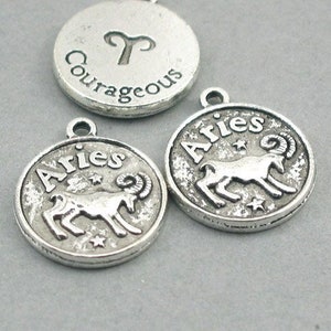 May include: Three silver charm pendants with the zodiac sign Aries. One pendant has the word "Aries" and a ram, another has the word "Aries" and a ram, and the third has the word "Courageous" and the Aries symbol.