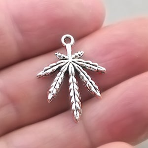 May include: Silver charm in the shape of a marijuana leaf. The charm is detailed and has a realistic look.